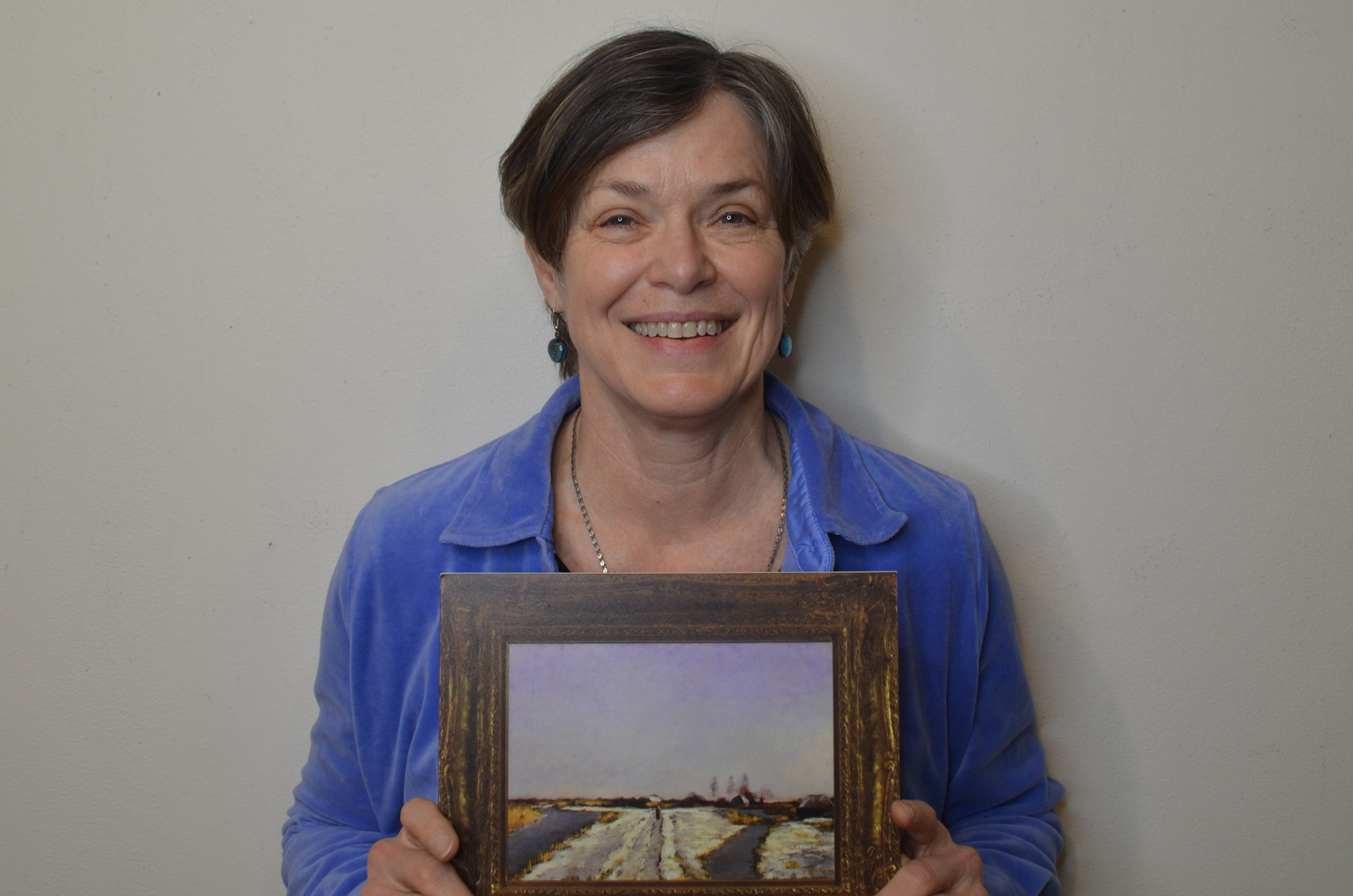 Photo of Cory Gooch, a woman with short hair, smiling and holding a small image of a painting