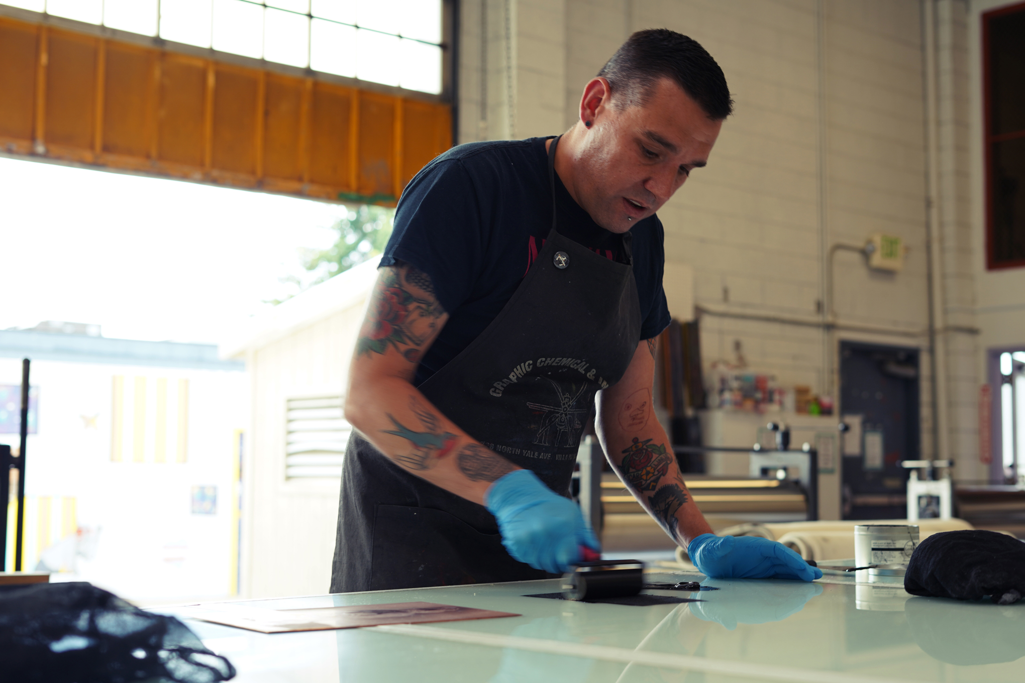 Photo of Ben Moreau, a man with short dark brown hair, rolling ink out in a print shop