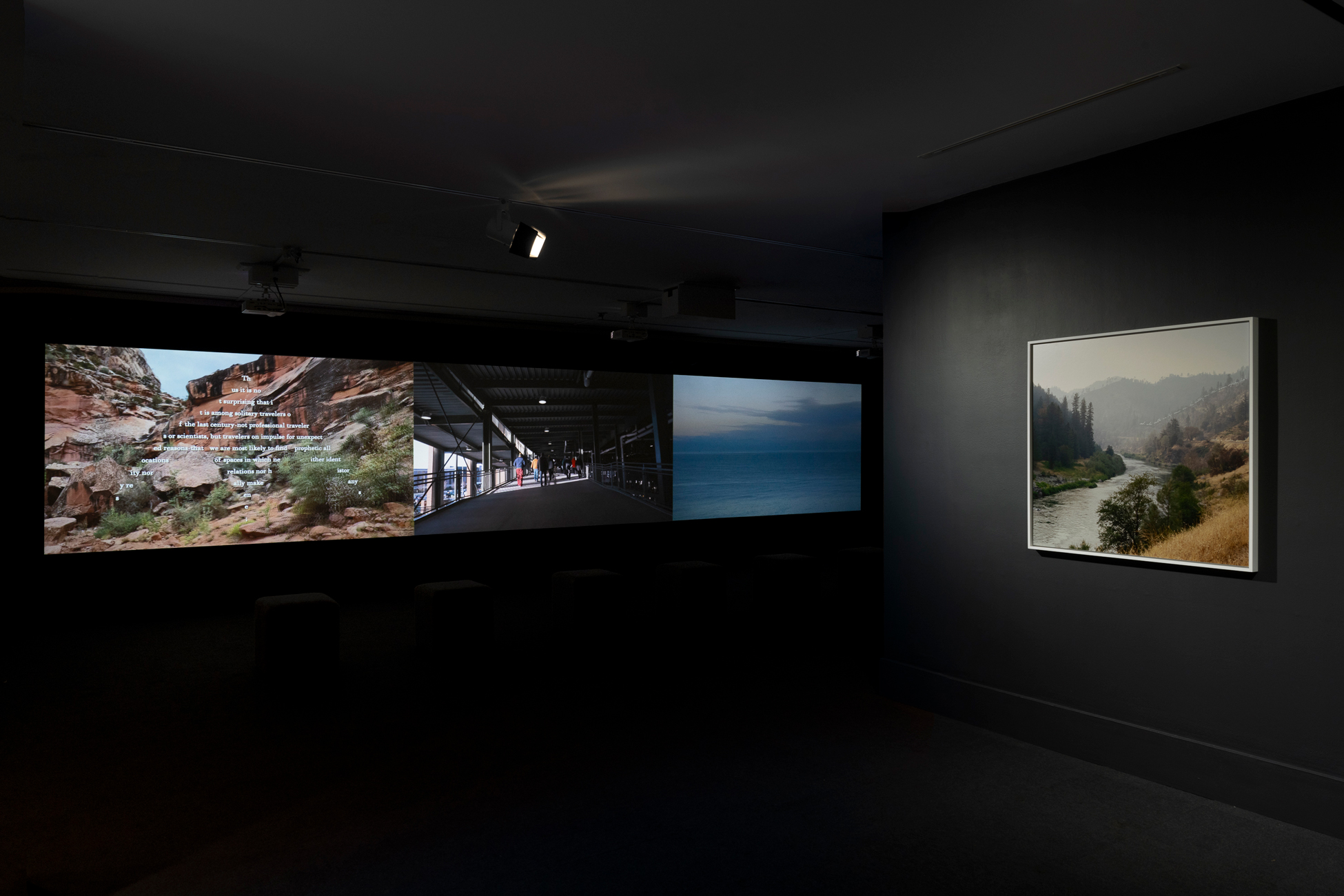 Photo of a video work and a photograph by Sky Hopinka in a dark gallery