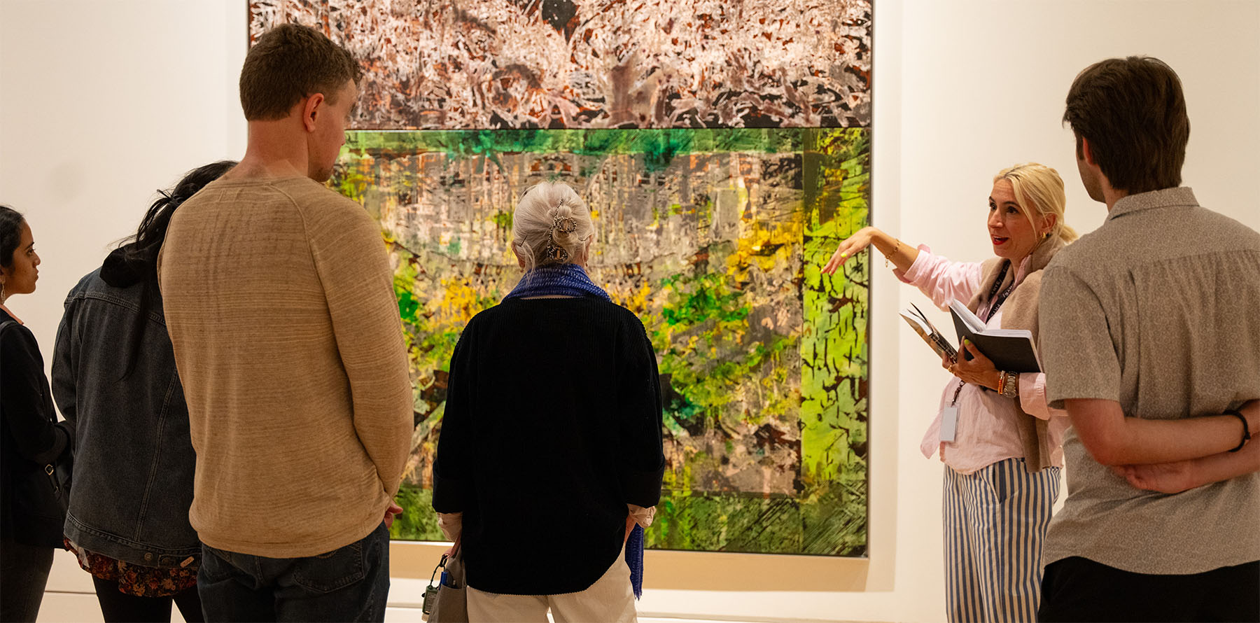 A woman standing next to a large abstract painting and speaking to a small group of people