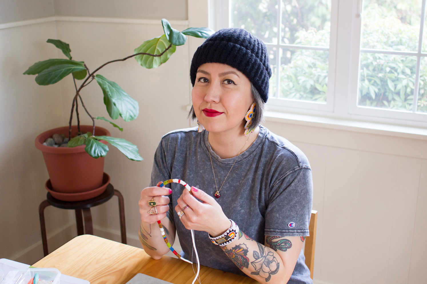 Photo of artist Naomi Parker sitting at a table and holding beading in her hands