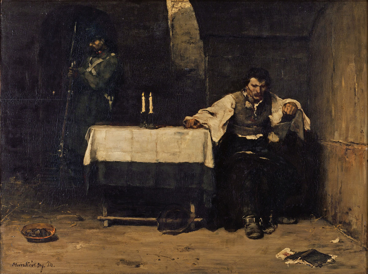 A man sitting at a small table light by candles in a stone cell