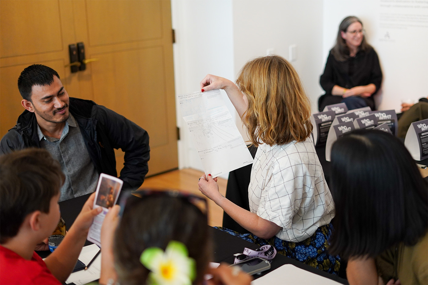 A person holding up a paper with instructions for a group seated at a table