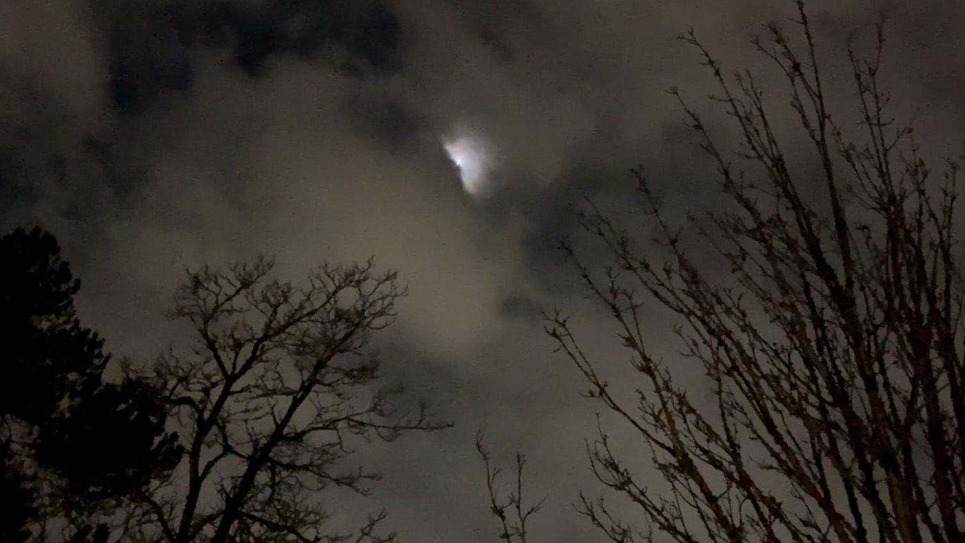 The moon is peeking out behind clouds and illuminating the scene