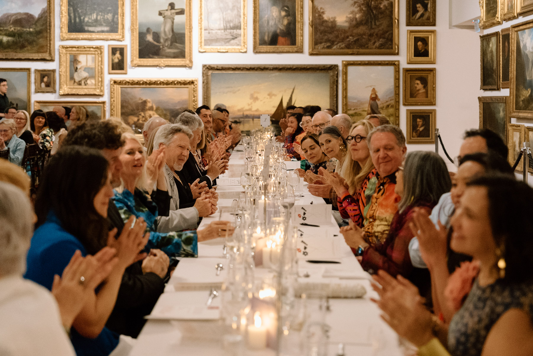 People seated at a long, formally set table in a large gallery space