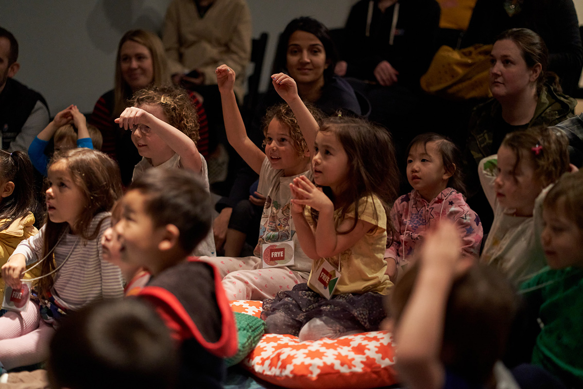 A group of children seated on the floor listening to and reacting to a speaker