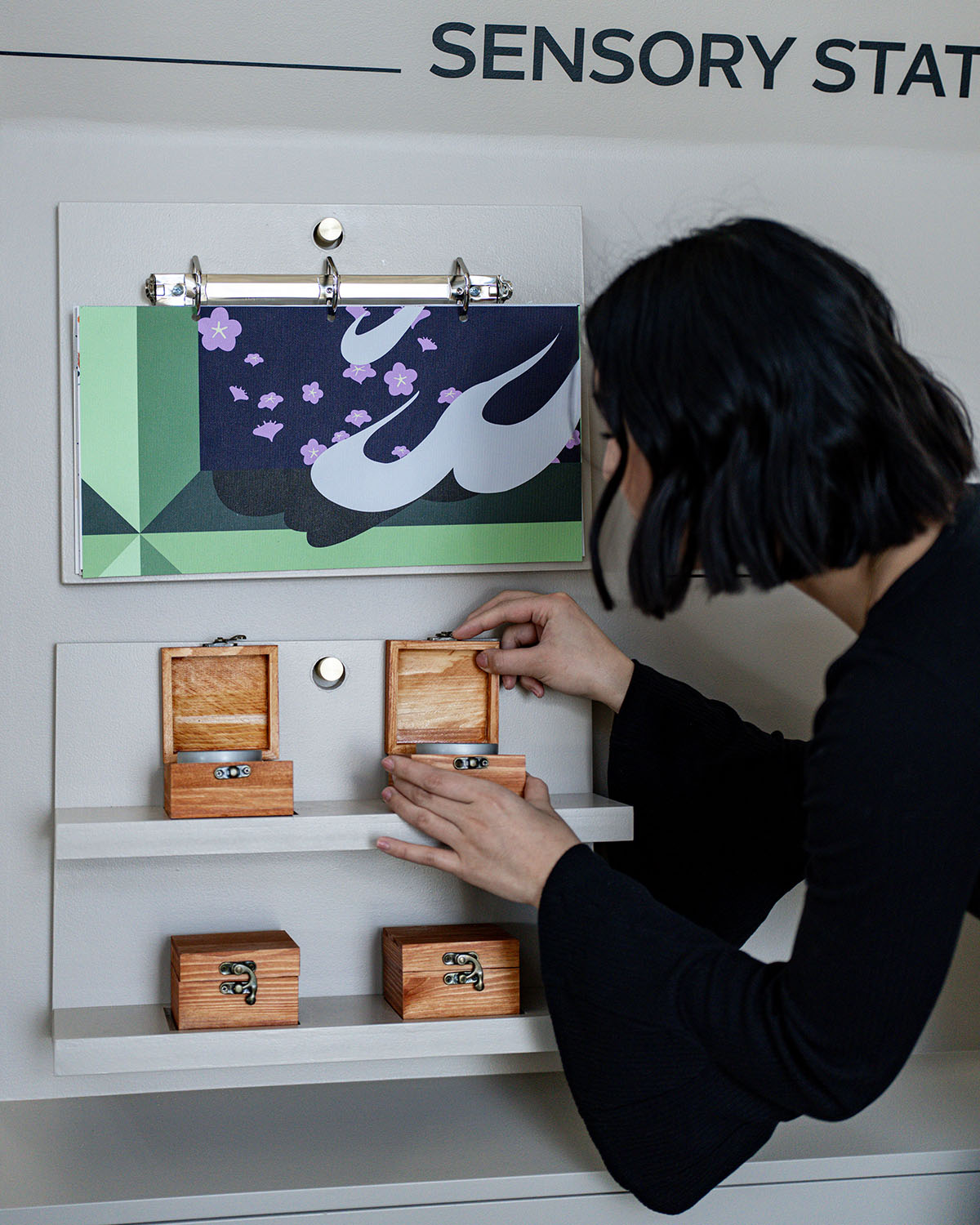 A person leaning over to look at an item in a small box on a mobile cart with the test 'Sensory Station'