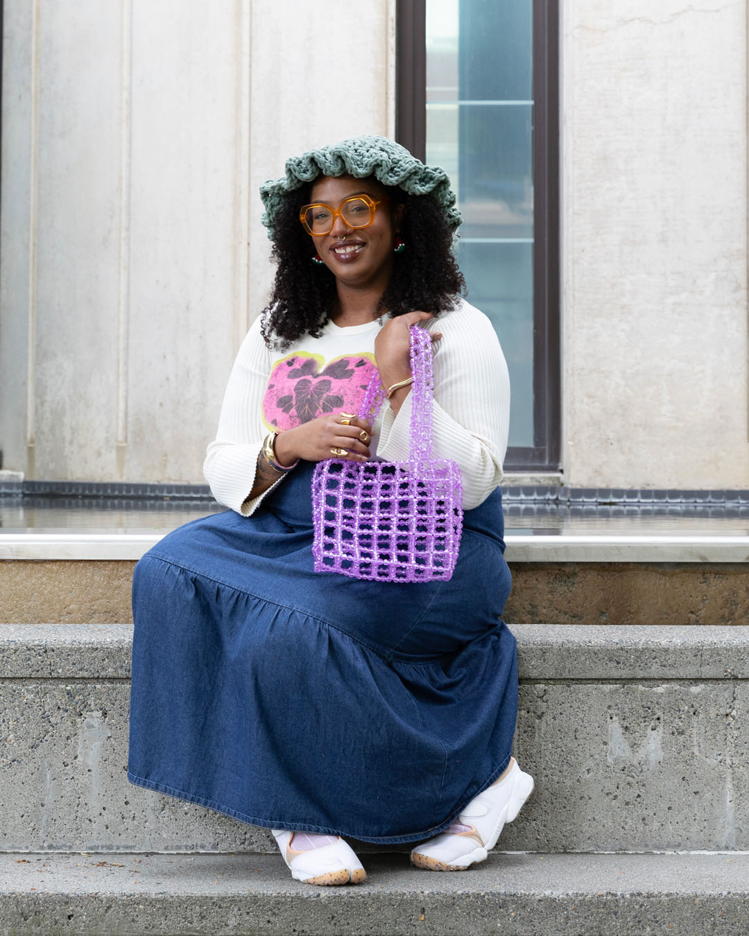 A person sitting on large concrete steps holding a purse made of clear purple beads