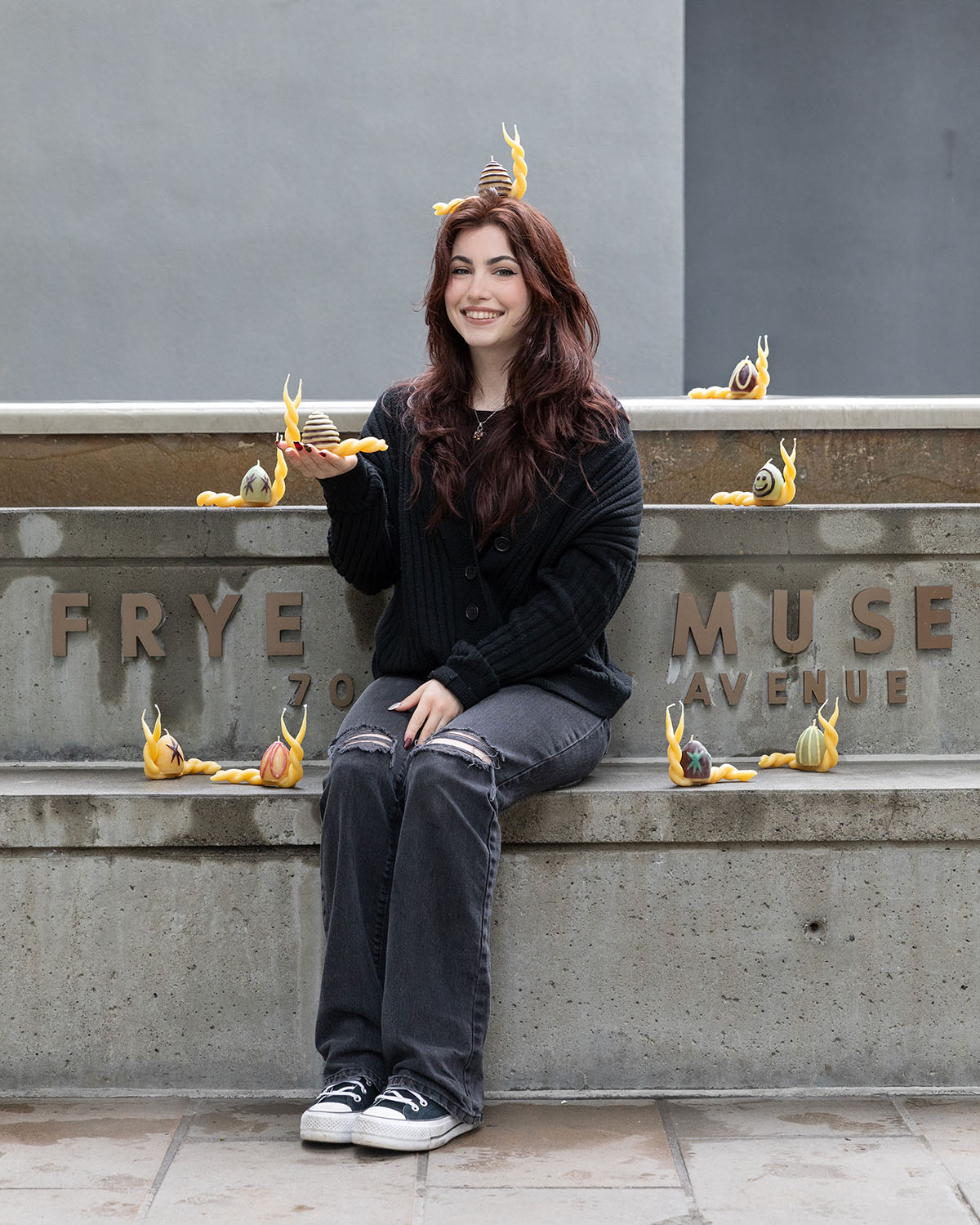 A person sitting on large concrete steps surrounded by wax candles in the shape of large snails