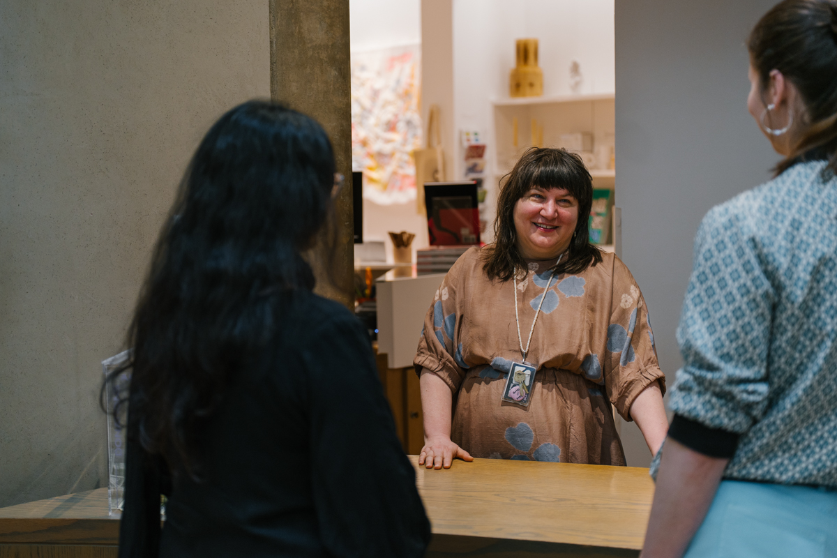 A person standing behind a desk smiles at two people she is talking to