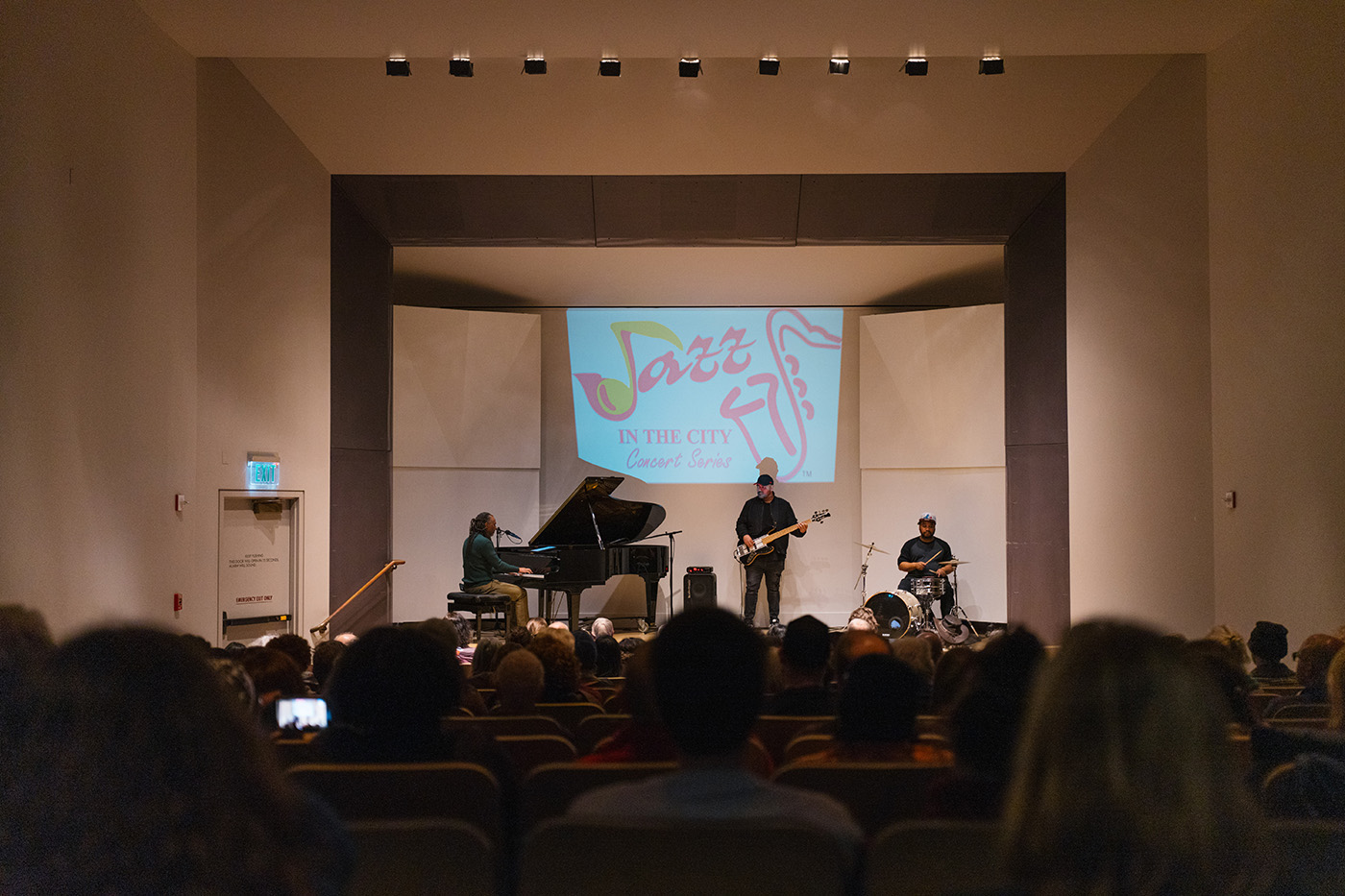 A trio of musicians performing on stage in front of a seated crowd.