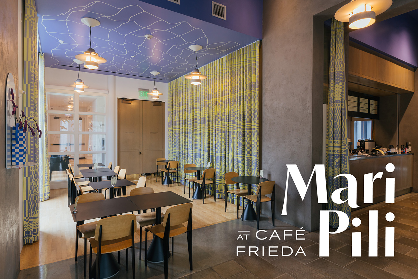 A well lit, empty cafe interior with yellow curtains and a painted blue ceiling. Text in the corner reads 'MariPili at Café Frieda'