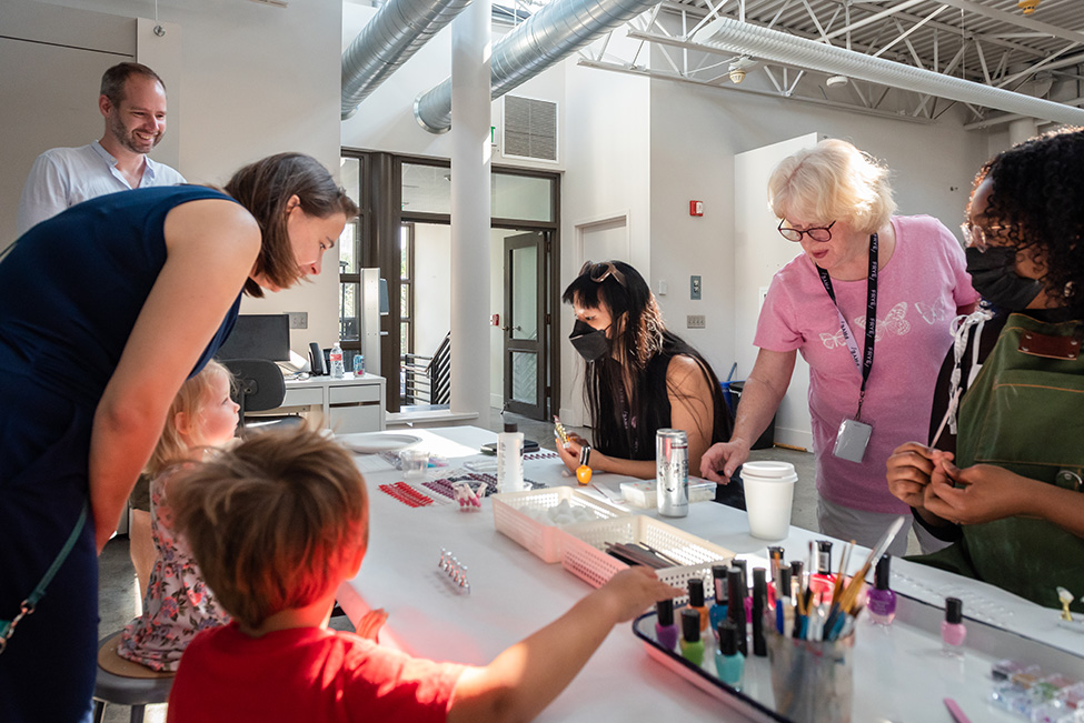 Adults and children work on an art activity around a table in a sunny, well lit studio space