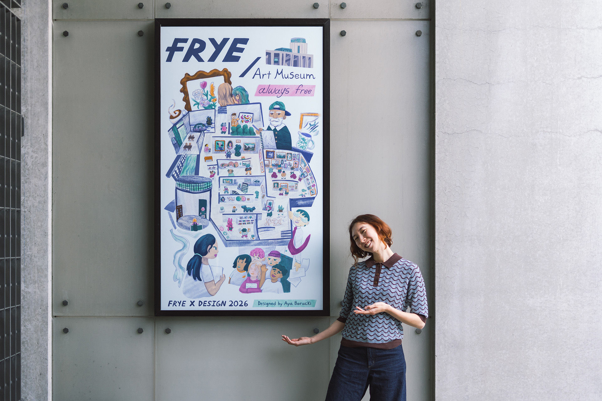 A person standing and smiling while holding their arms out to frame a large, illustrated poster installed on an outdoor wall