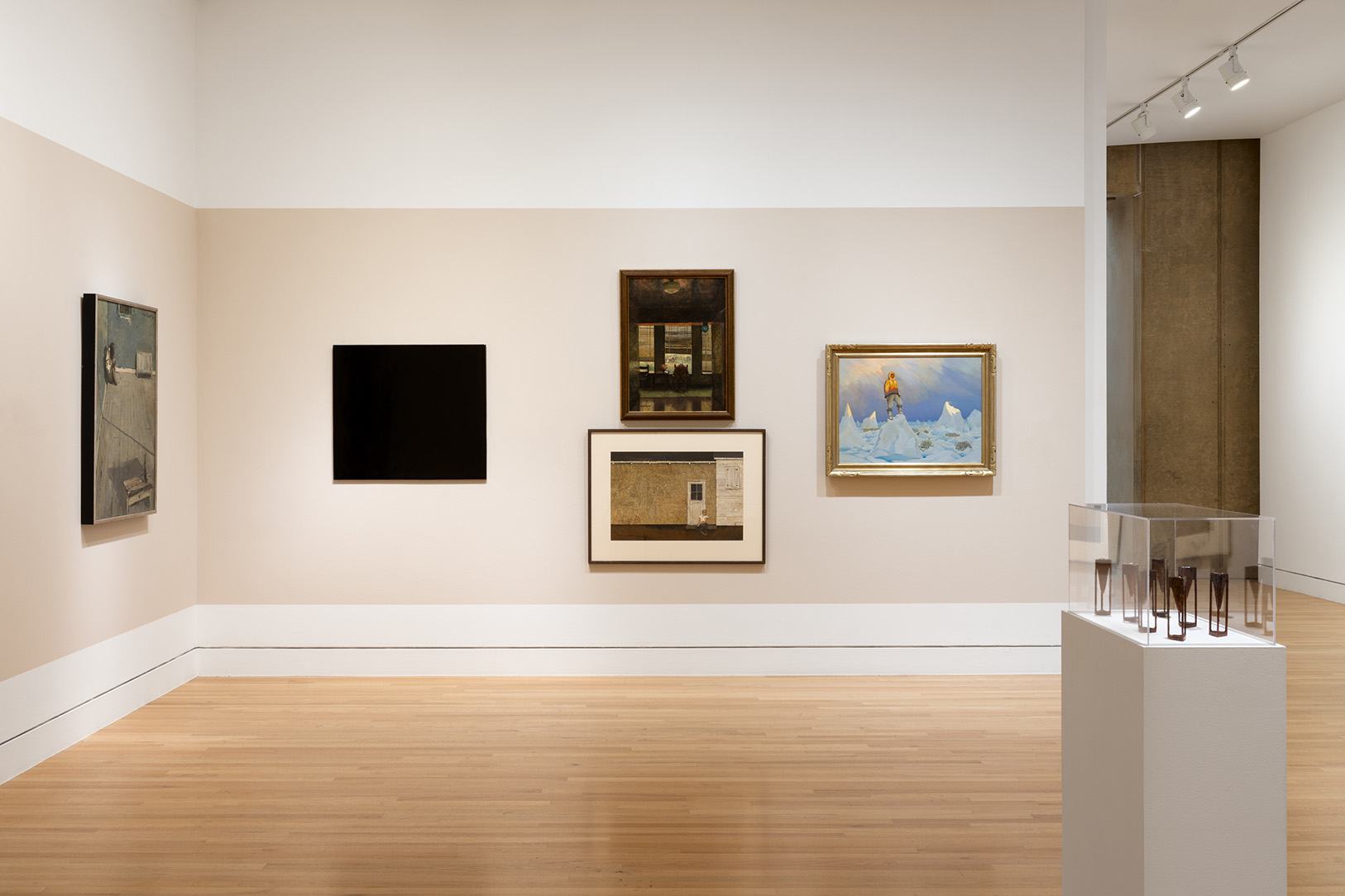 A corner of a gallery space with a number of flat artworks, plus a pedestal holding small three dimensional sculptures
