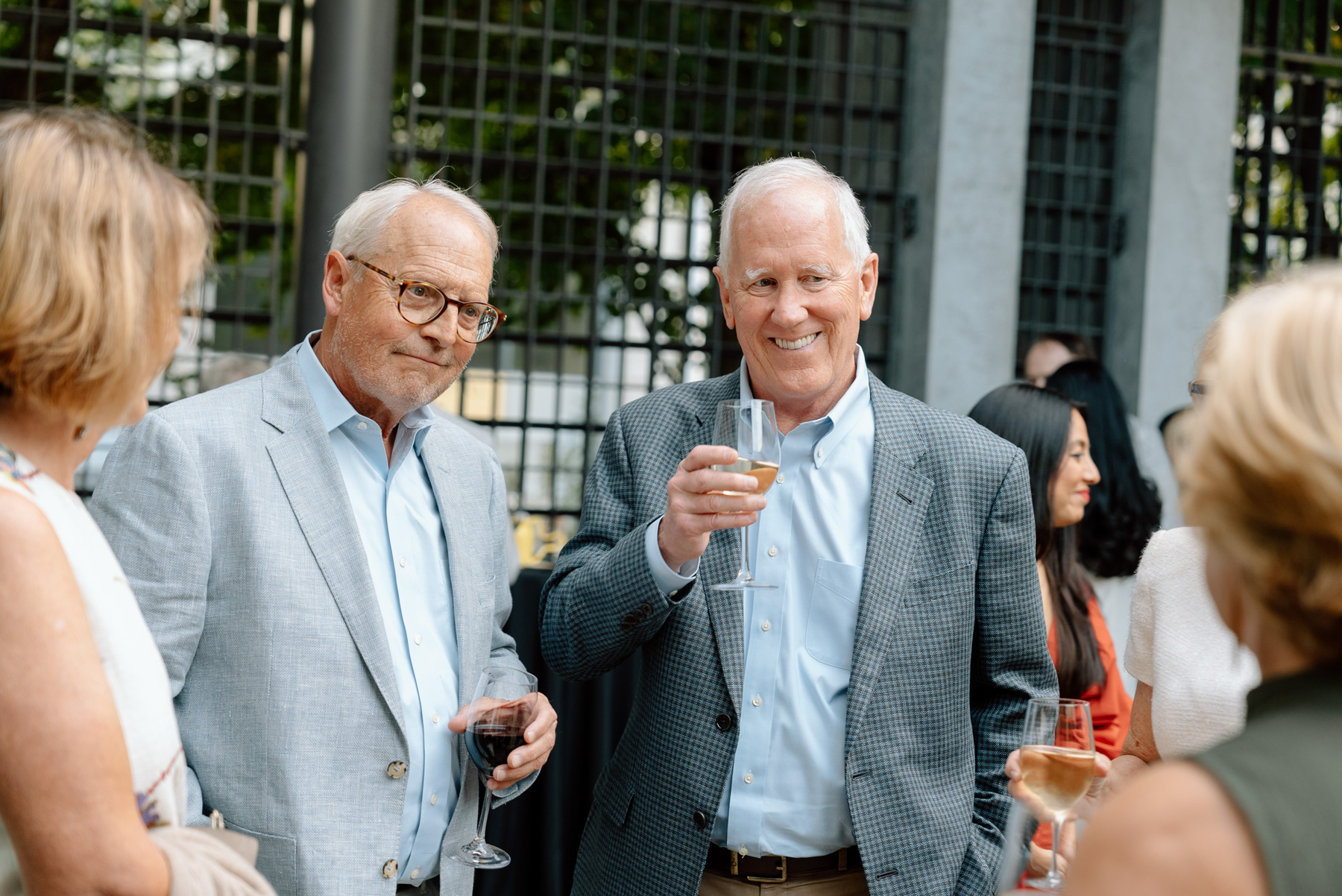 A small group of people in a busy courtyard in cocktail party attire smiling and chatting