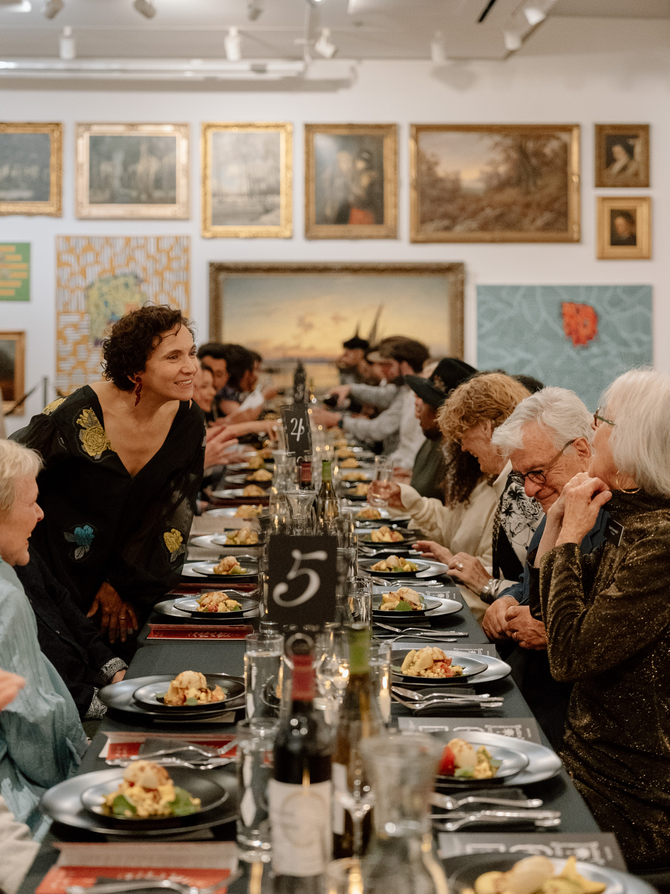 People sitting down to a formal dinner at a long table in an art gallery space