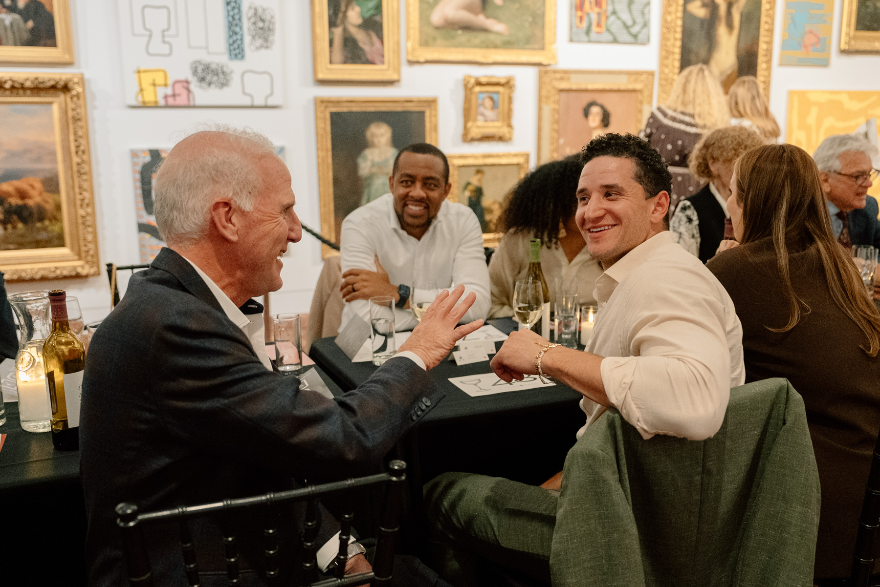 A small group of people chatting across a long table in a gallery space