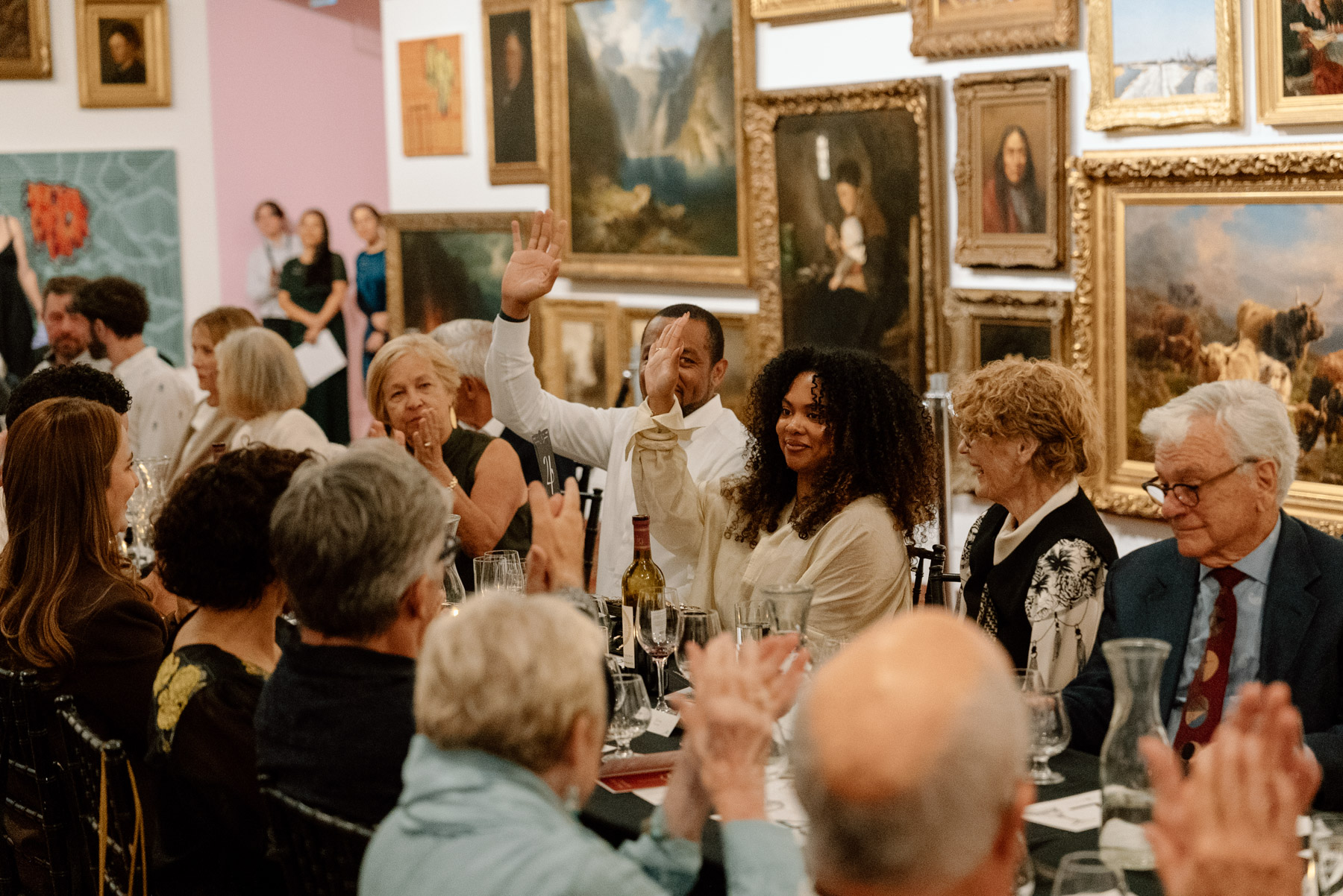 People at a long table in an art gallery space. A few are raising their hands