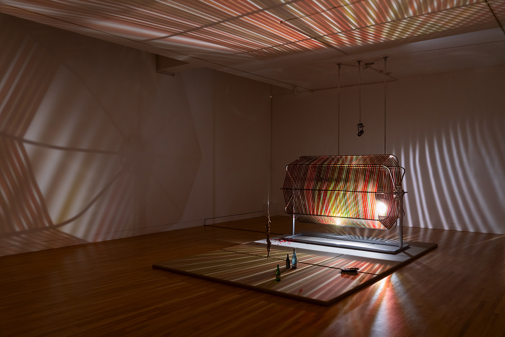 A large gallery space illuminated by a three dimensional artwork with light shining through thing strips of rotating film