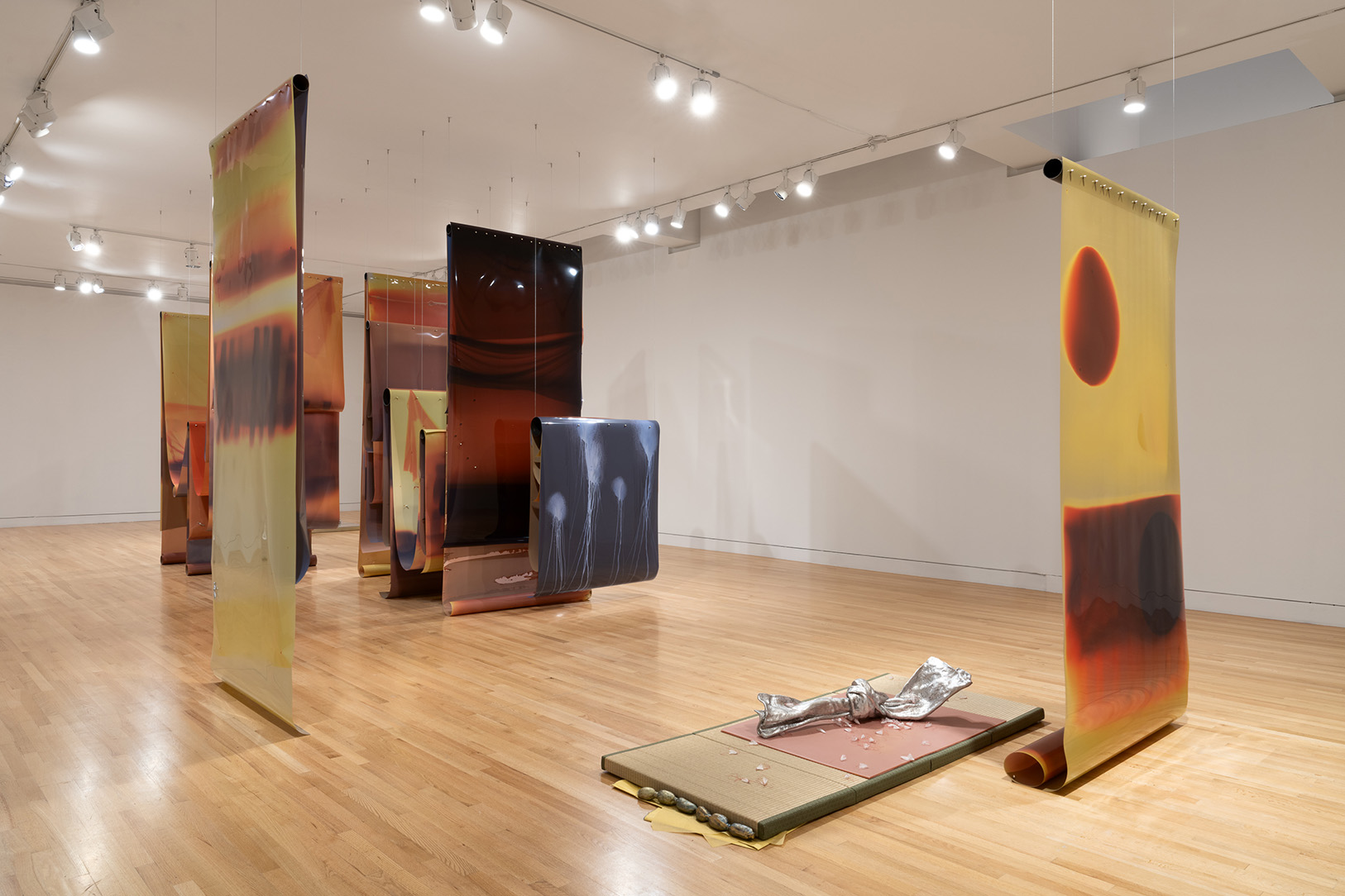 A large gallery space with large sheets of vertically suspended material in orange and yellow