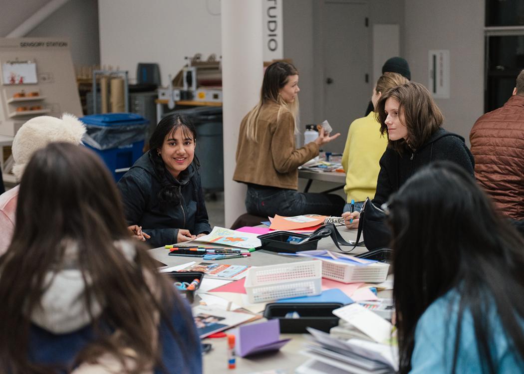 People sitting around a large table covered in art supplies and chatting
