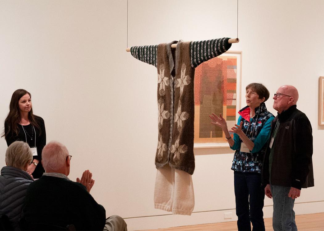 People standing around and talking about a suspended textile artwork