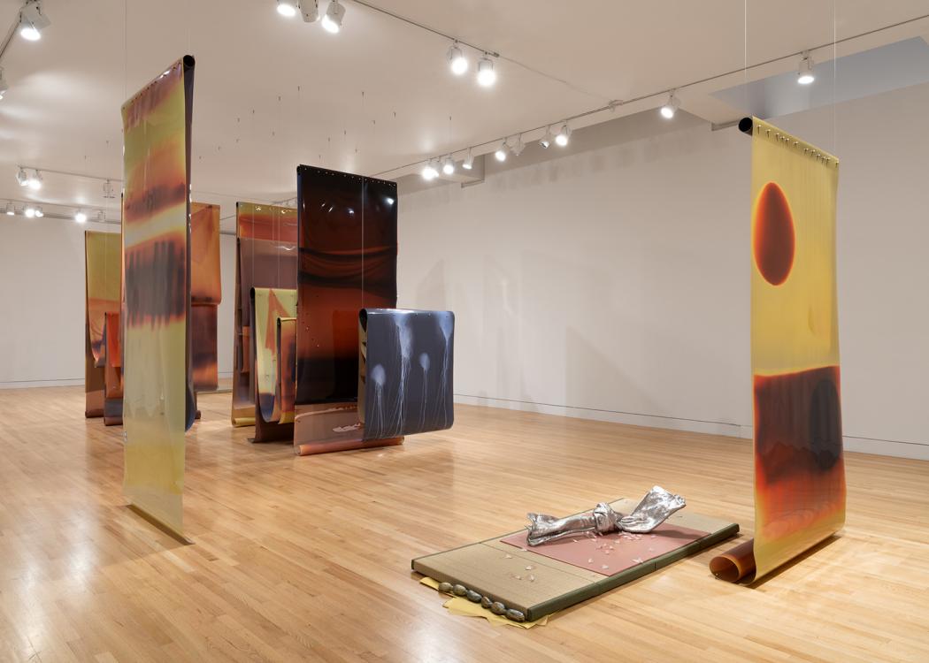 A large gallery space with large sheets of vertically suspended material in orange and yellow
