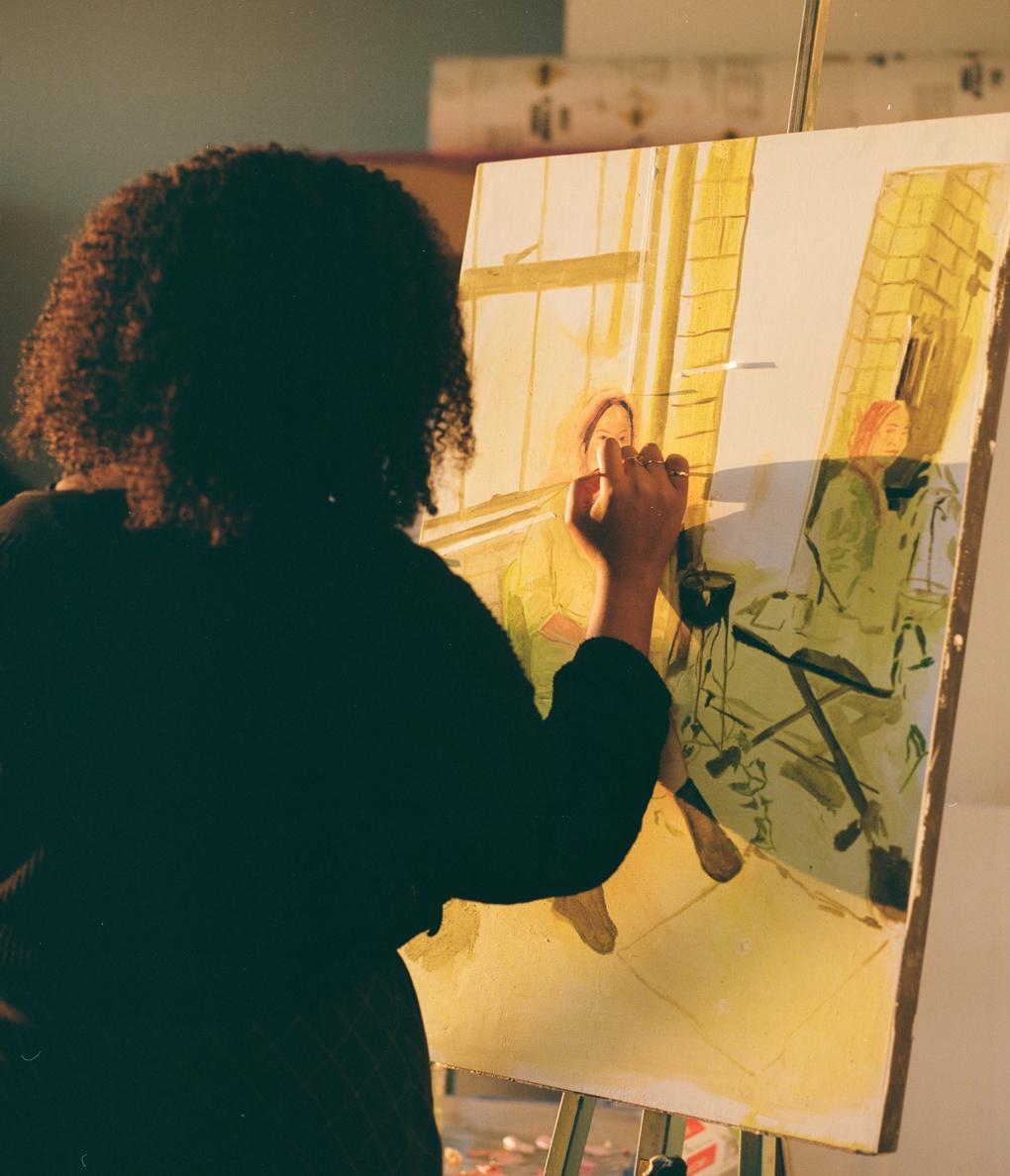 Photo of Lila Thomas from behind while she paints on a canvas