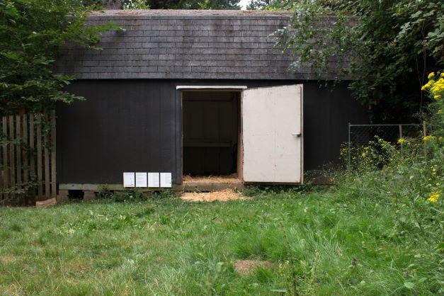 Small black wooden building with white door adjar