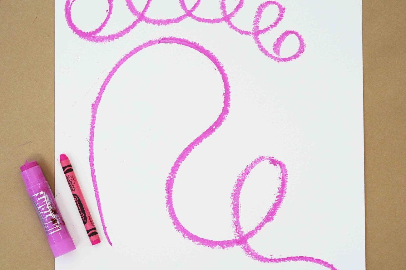 Photo of a sheet of paper with pink squiggles drawn on it and a pink crayon and pastel sitting on top of the paper