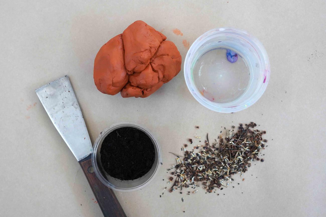 Photo of supplies for the art activity including clay, seeds, a cup of water from above