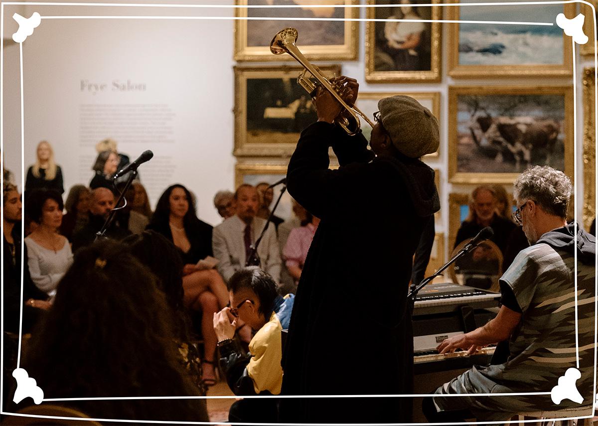 A person playing an instrument for an audience in a large room. There is a white designed outline drawn on top of the image