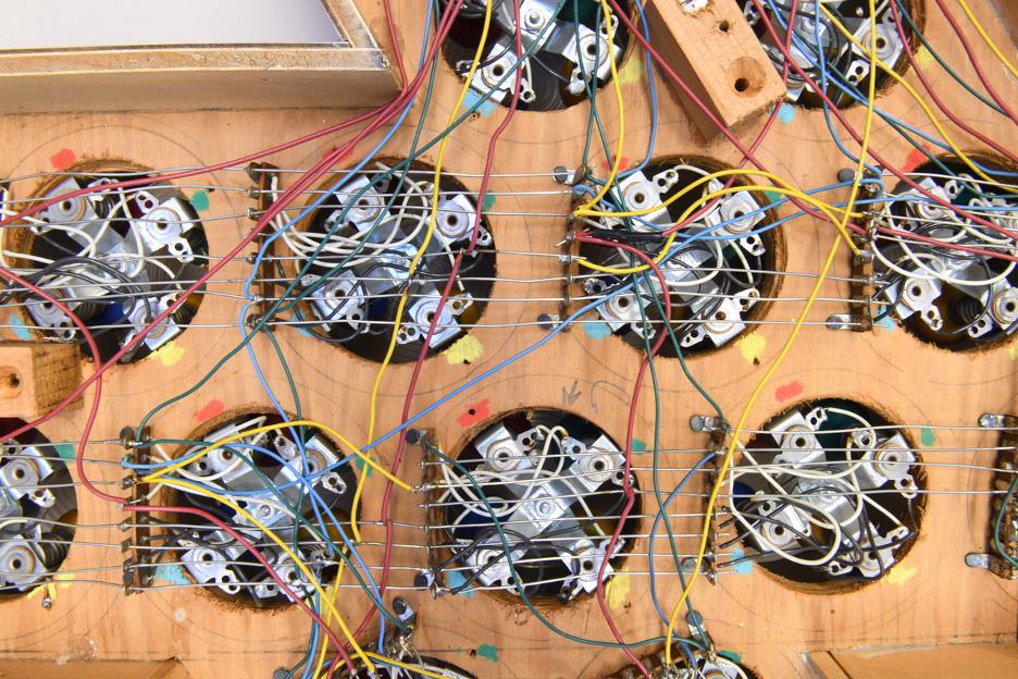 A view of a number of electrical circuits in cicular pockets on a piece of wood connected by wire