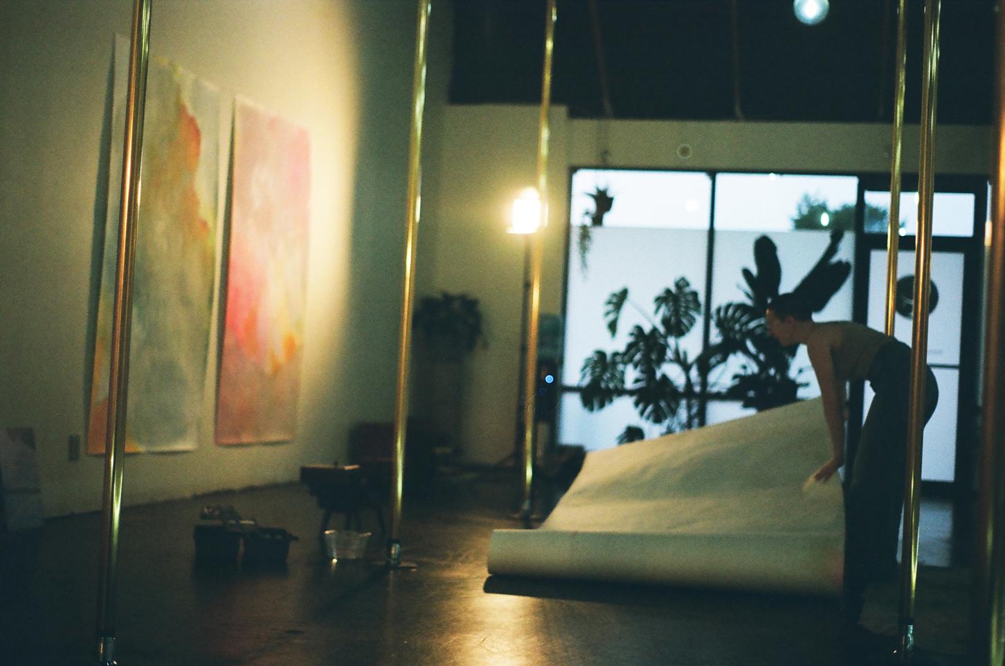 Photograph of Lydia Jewel Gerard laying out an artwork on the ground among gold poles in the Lilith Pole studio