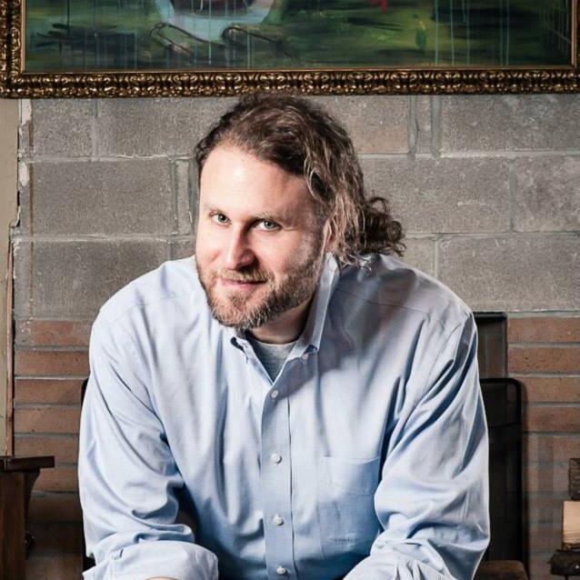 A person in a button up shirt sitting on a bench and leaning forward