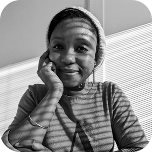 A black and white image of a woman with light and shadow from window blinds being cast upon her