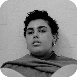 A black and white photo of a person sitting and leaning back against a white brick wall