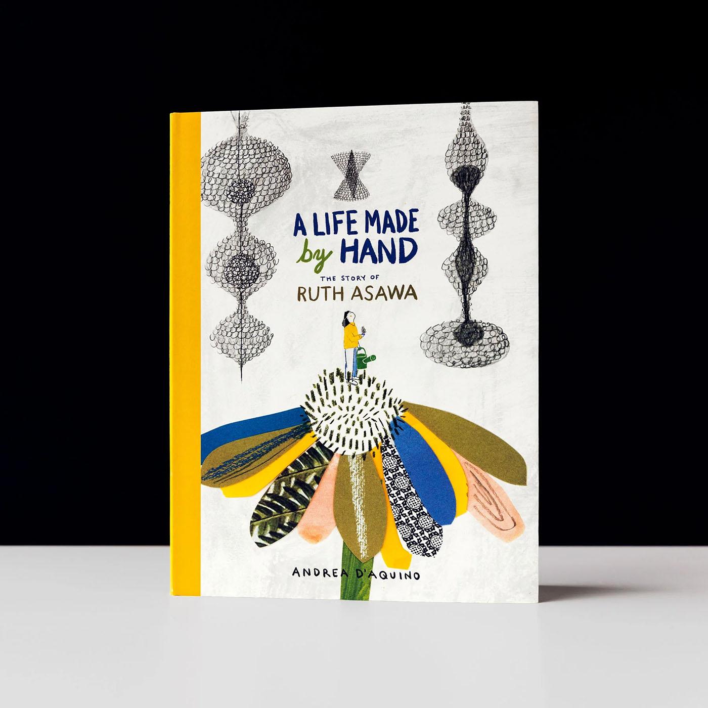 A book on a white table, the cover has an illustrated flower and metal hanging artworks and the text 'A Life Made by Hand: the Story of Ruth Asawa'