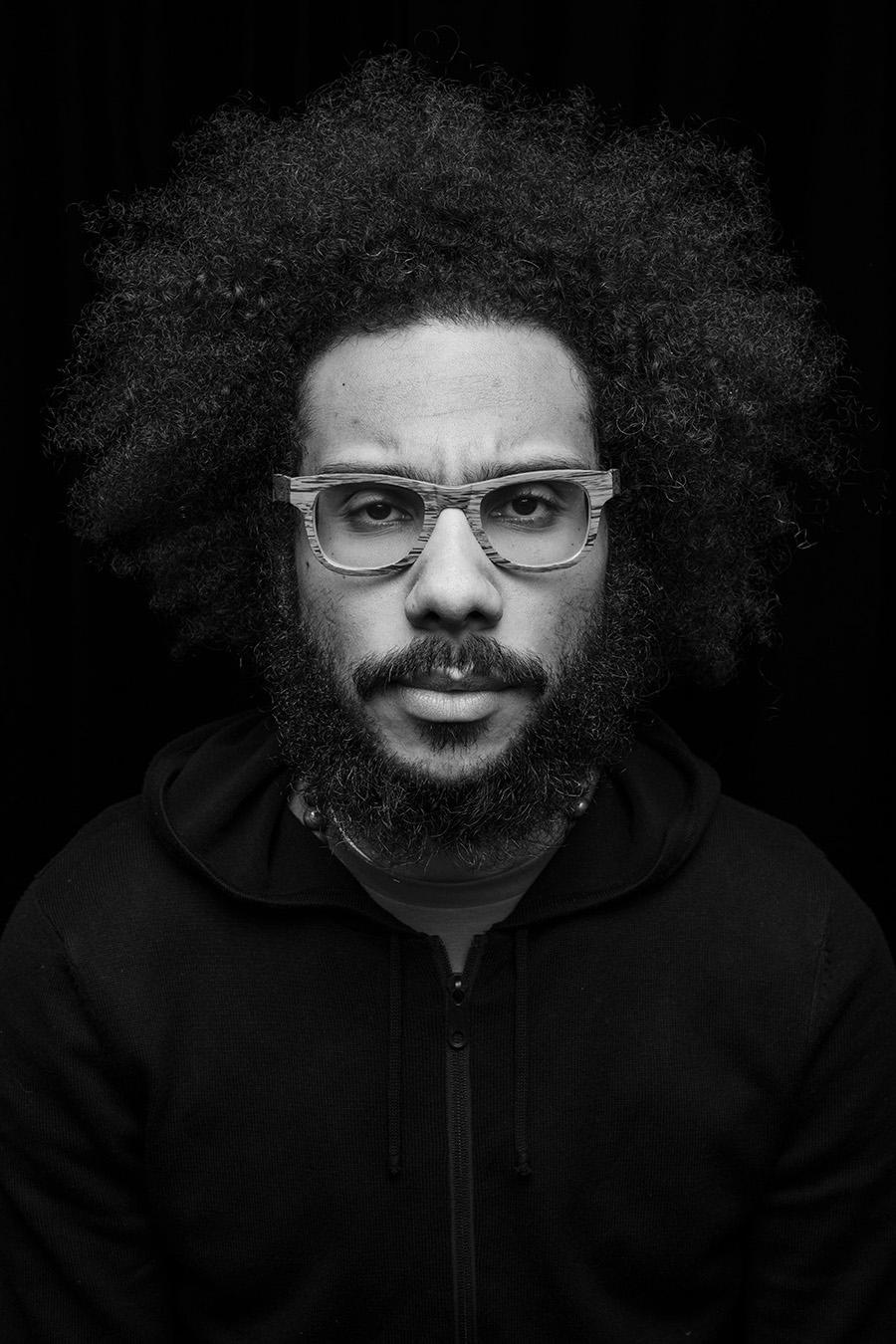 A black and white portrait photo of a man with an afro and beard wearing glasses
