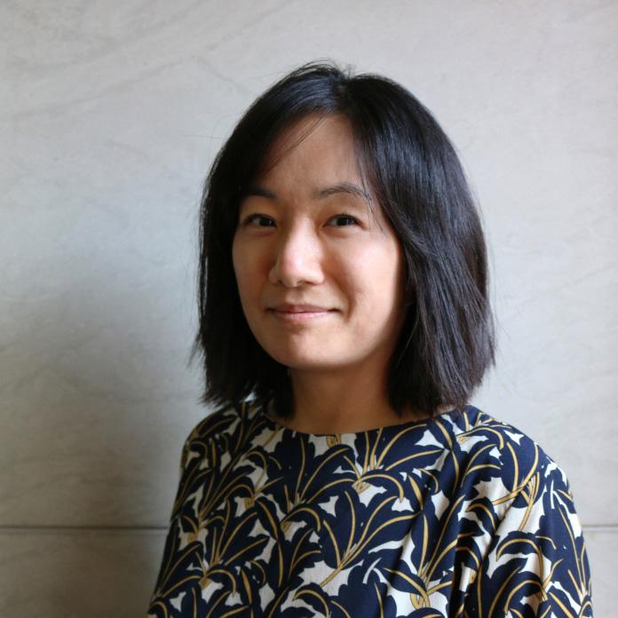 A woman with medium length dark hair standing in front of a white wall