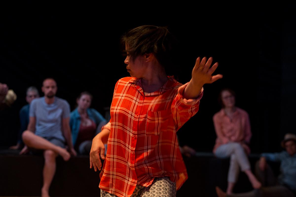 A person in a red patterned shirt dancing in front of a seated audience