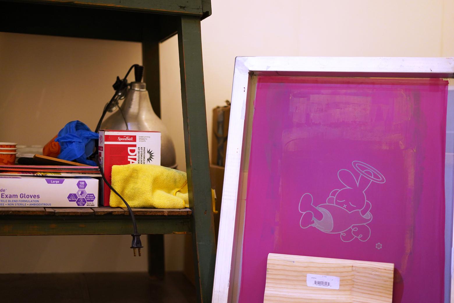 A screenprinting screen with a small character on it next to a shelf with materials