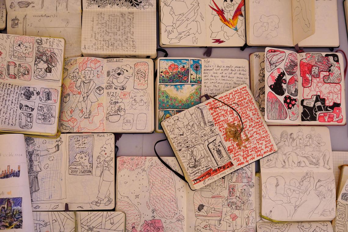 Many journals with drawings and writing in them open on a tabletop