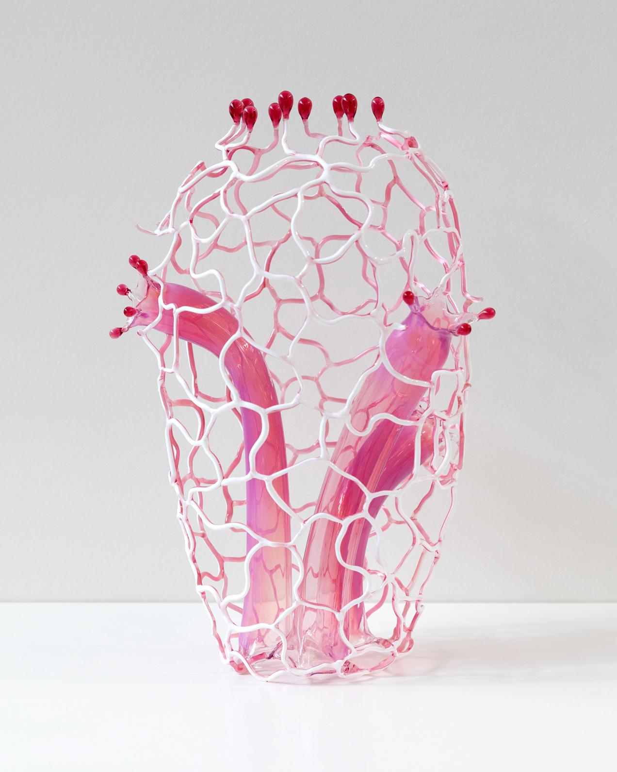 A pink, white, and red glass art piece with thing squiggling pieces which make the general shape of a vase but look very biological in nature