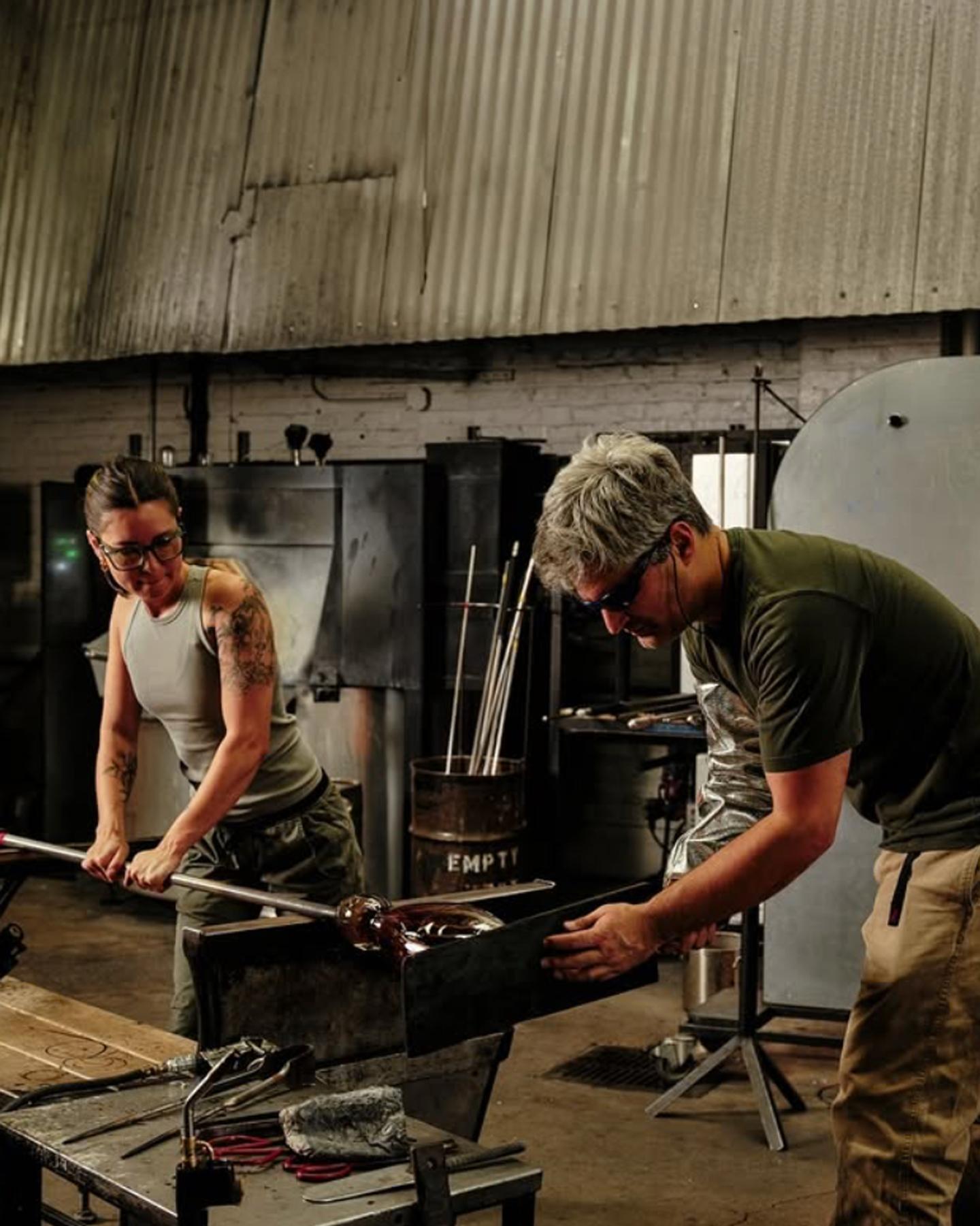 Sue Kim and Zeke Spier working together on a glass art piece in a hot shop