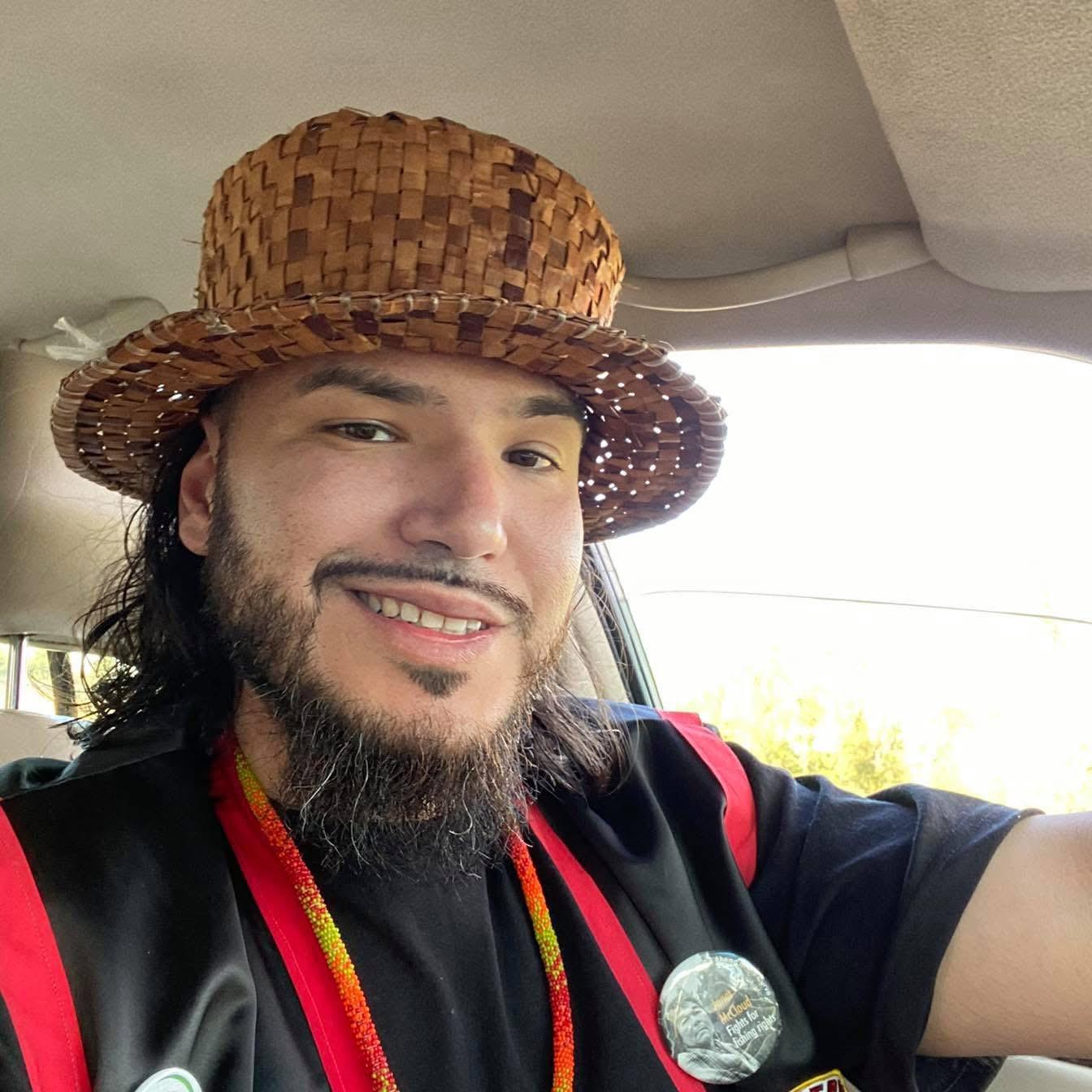 A man with a beard sitting in a car and wearing a hat with a circular brim made of organic materials