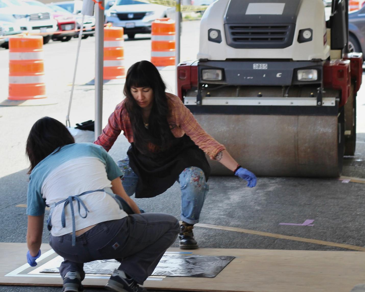 Artists Saiyare Refaei and Yoshi Nakagawa squatting next to an artwork working