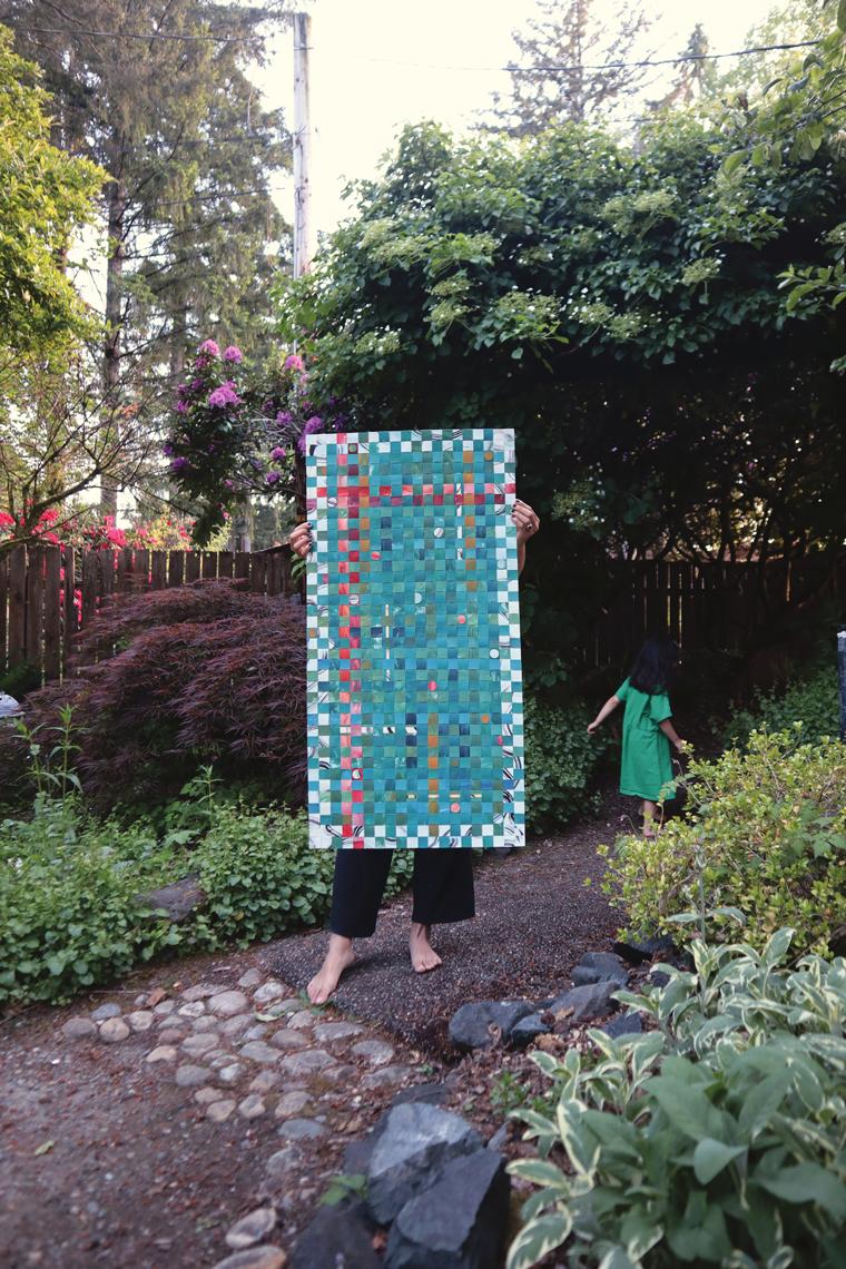 lexa toledo villanueva's woven paper artwork being held up by a person in a lush outdoor environment