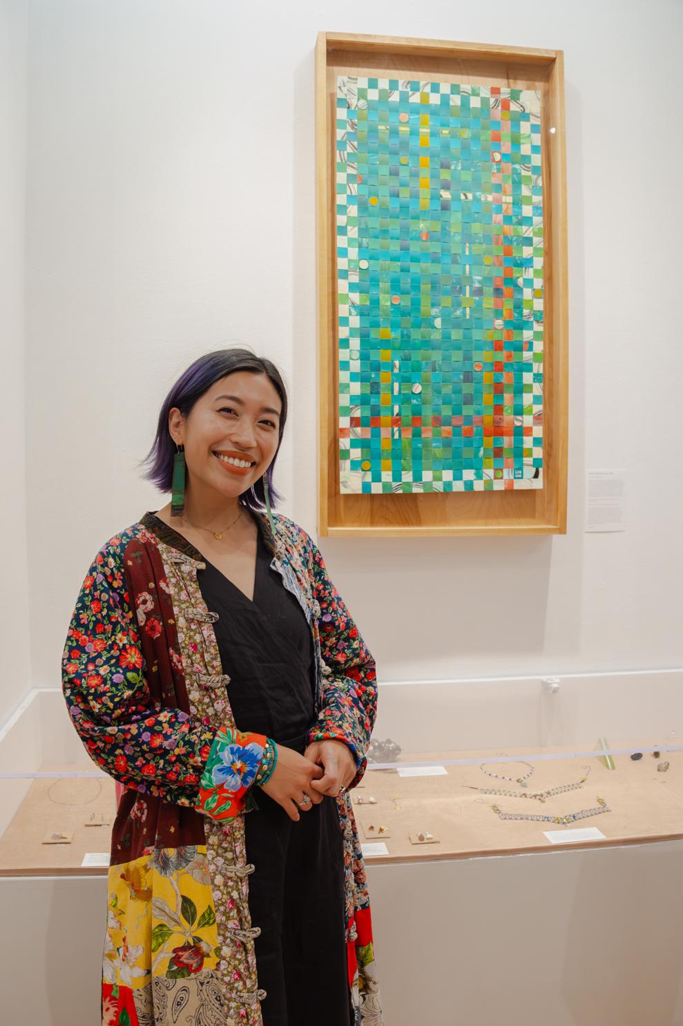 lexa toledo villanueva stands smiling in a black dress and colorful jacket beside her woven artwork "From Cavite With Love" hung in the Store's alcove